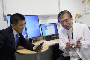 お互いのスマートをフォンの画面を見せ合う、市長とセンター長