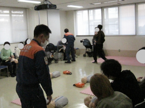 消防職員による救命処置の説明の様子。乳児の救命人形に、胸骨圧迫をおこなっている参加者が写っている。