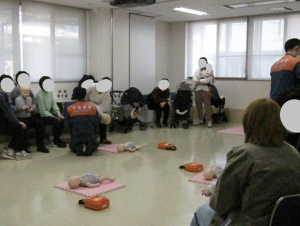 救命処置の講習の様子。子どもが誤飲した場合の対応を学ぶため、消防職員が小児の救命人形を使って、腹部突上げ法のやり方を説明している様子。