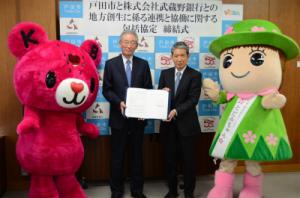 戸田市長と武蔵野銀行頭取、それぞれのマスコットキャラクターである、とだみちゃん、ドリームテイルクーベアの記念写真の画像